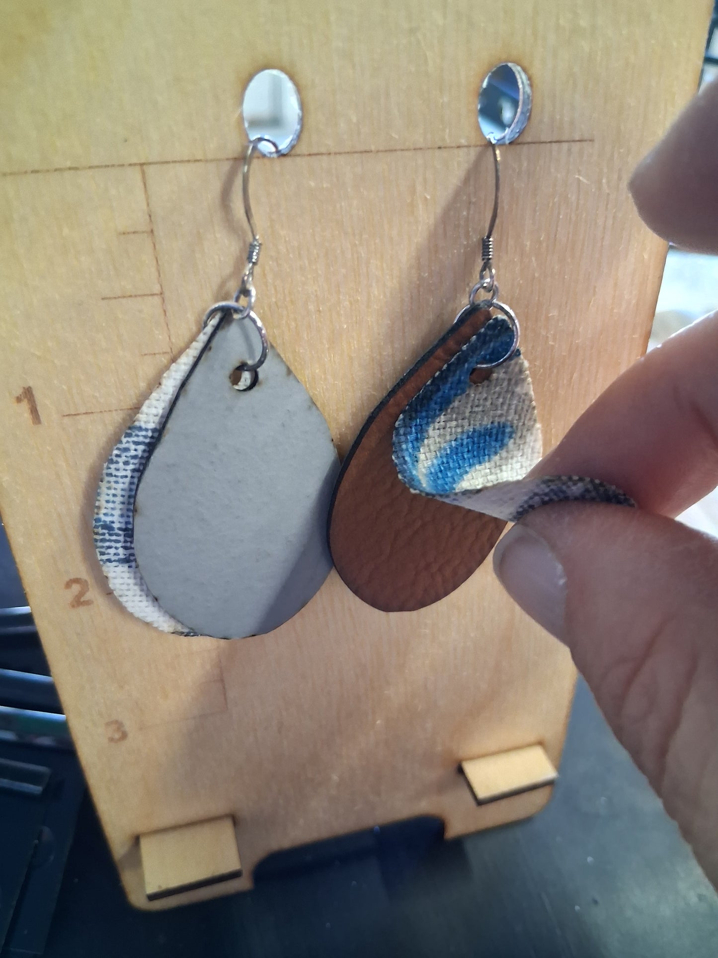 Pair of earrings with fabric in front of a pleather back on a wooden surface with a ruler for scale.