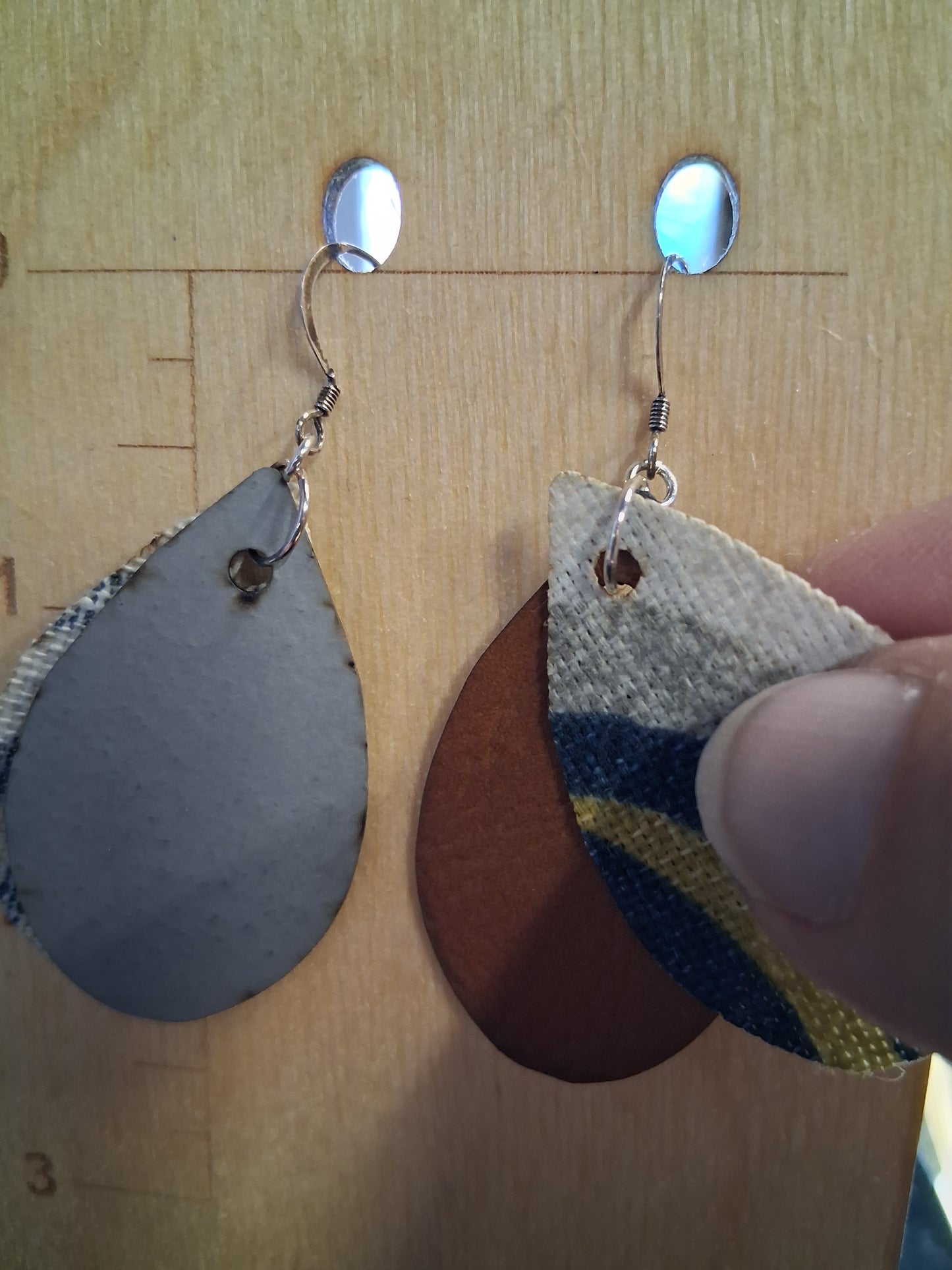 Pair of earrings with fabric in front of a pleather back on a wooden surface with a ruler for scale.
