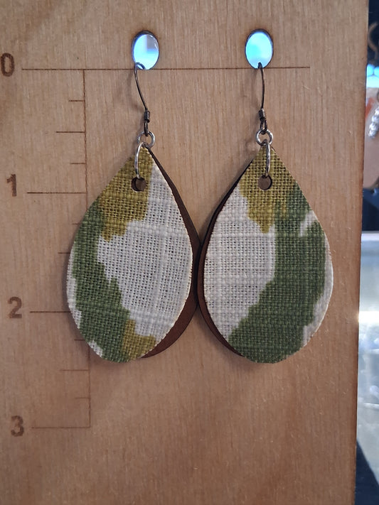 Pair of earrings with camouflage design fabric in front of a pleather back on a wooden surface with a ruler for scale.