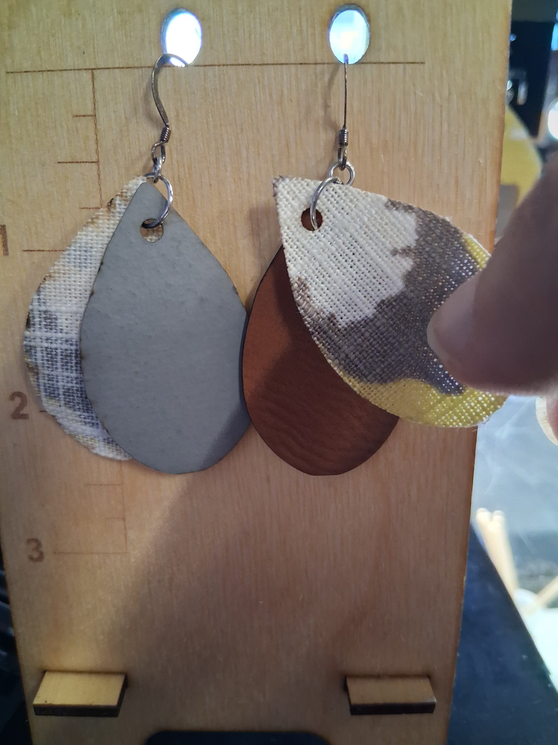 Pair of earrings with fabric in front of a pleather back on a wooden surface with a ruler for scale.