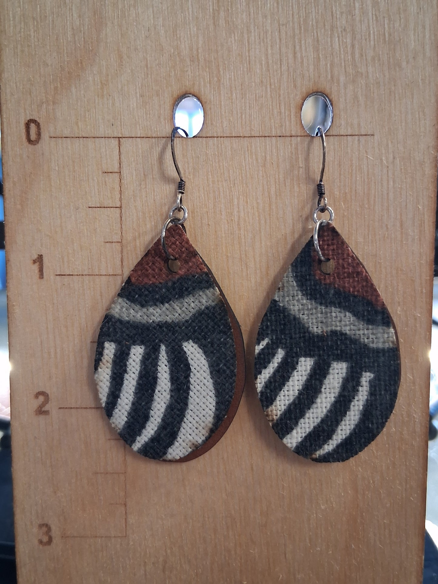 Pair of earrings with fabric in front of a pleather back on a wooden surface with a ruler for scale.
