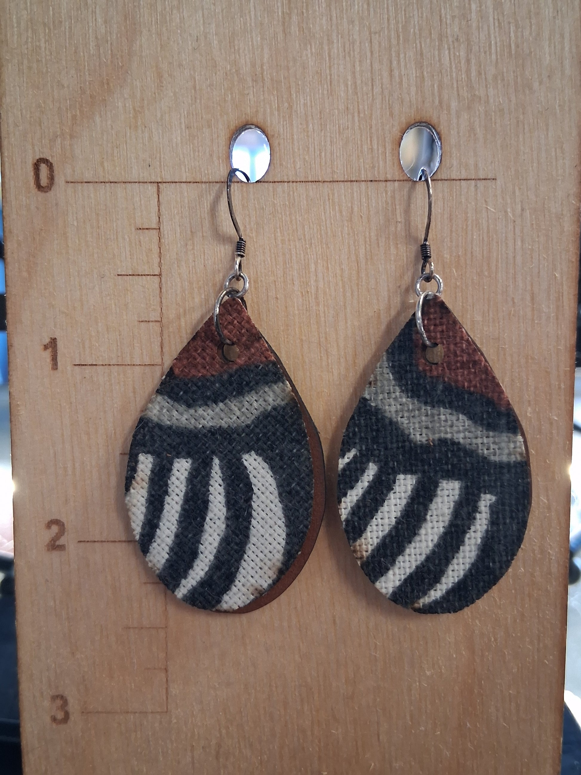 Pair of earrings with fabric in front of a pleather back on a wooden surface with a ruler for scale.
