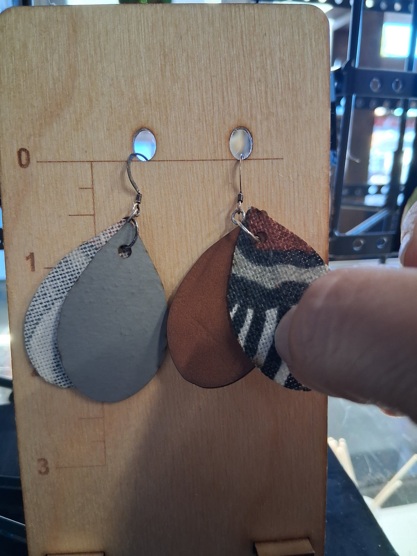Pair of earrings with fabric in front of a pleather back on a wooden surface with a ruler for scale.