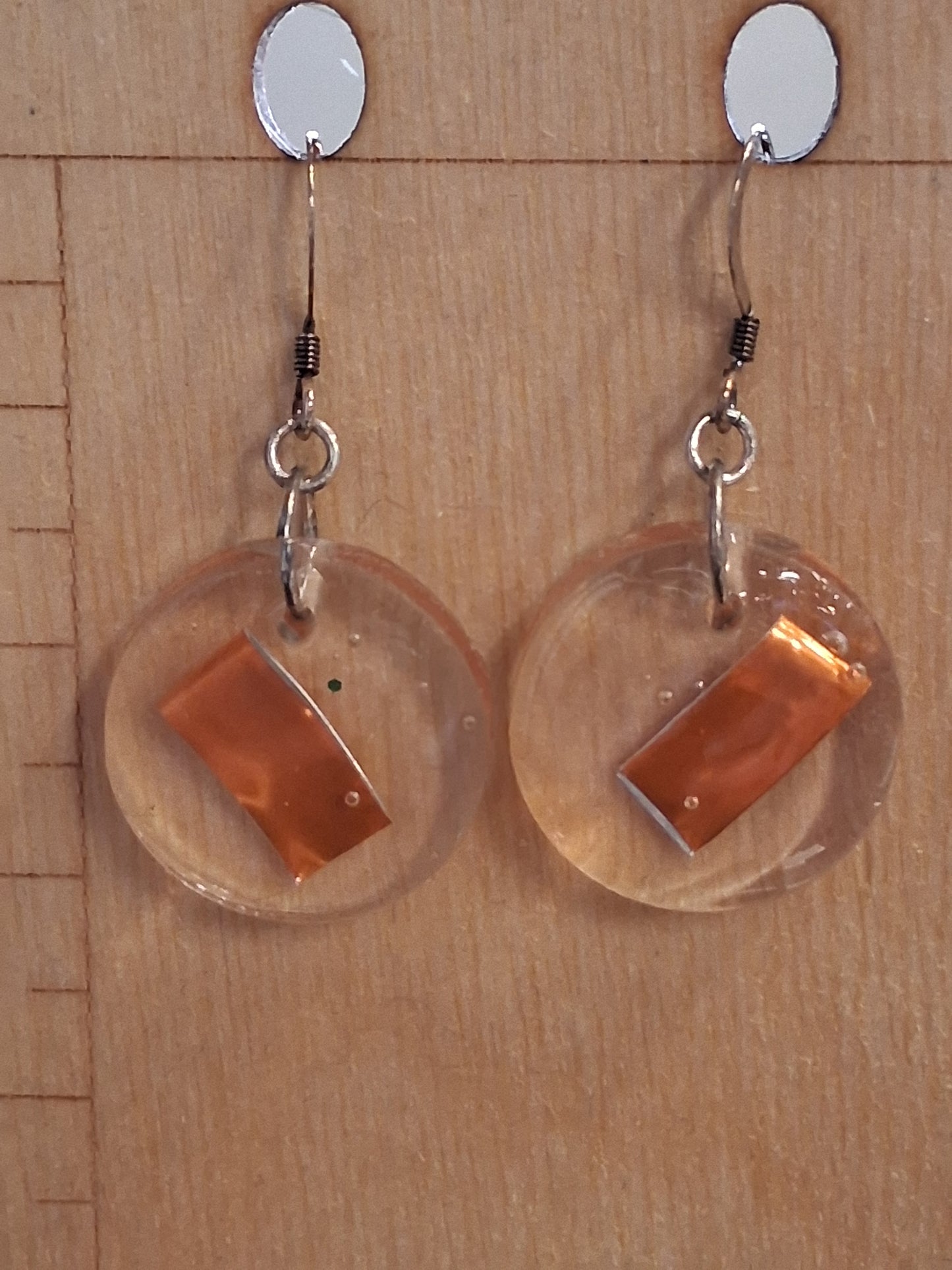 slices of orange aluminum cans suspended in resin made into earrings displayed on a wood background
