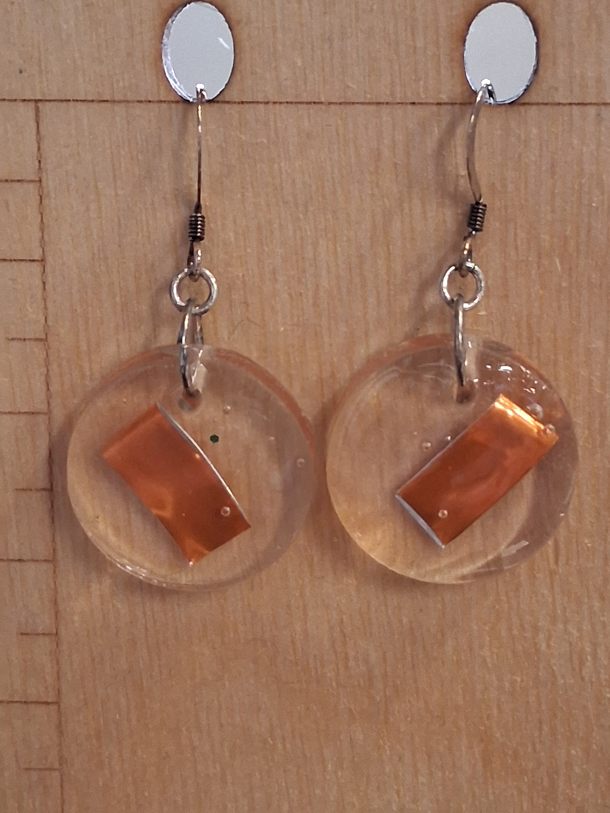 slices of orange aluminum cans suspended in resin made into earrings displayed on a wood background
