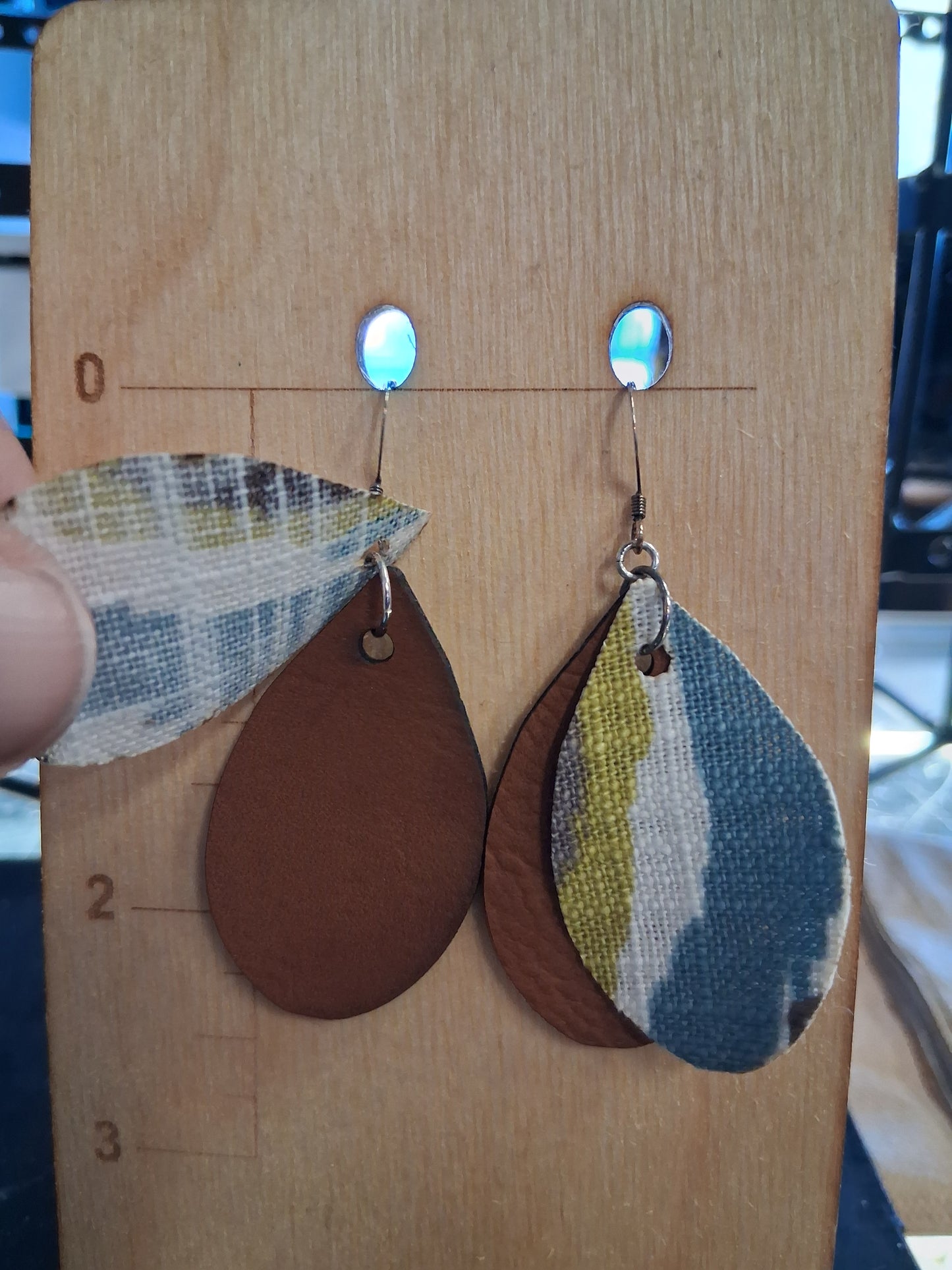 Pair of earrings with fabric in front of a pleather back on a wooden surface with a ruler for scale.