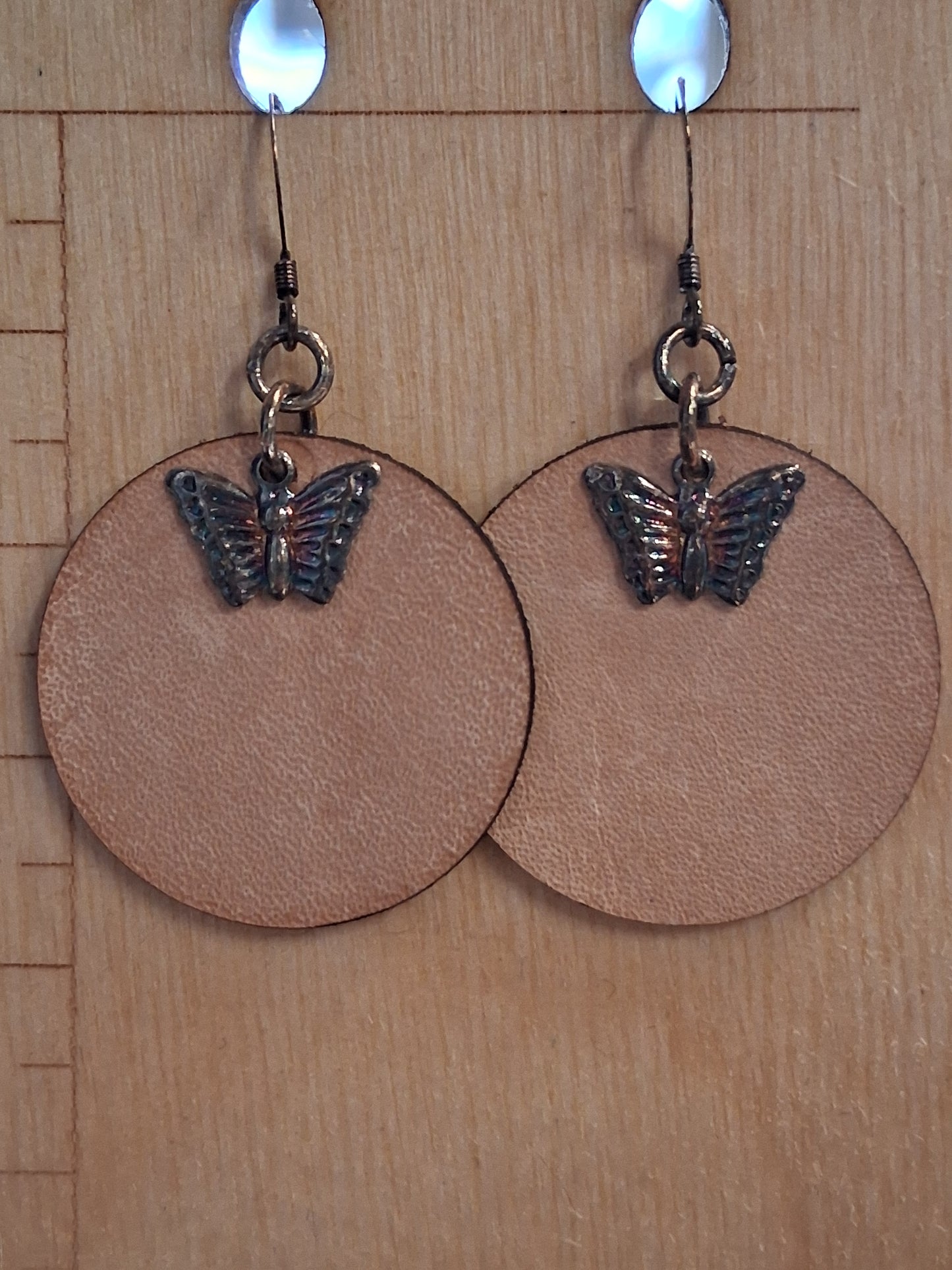 Leather earrings with butterfly charms on a wooden surface