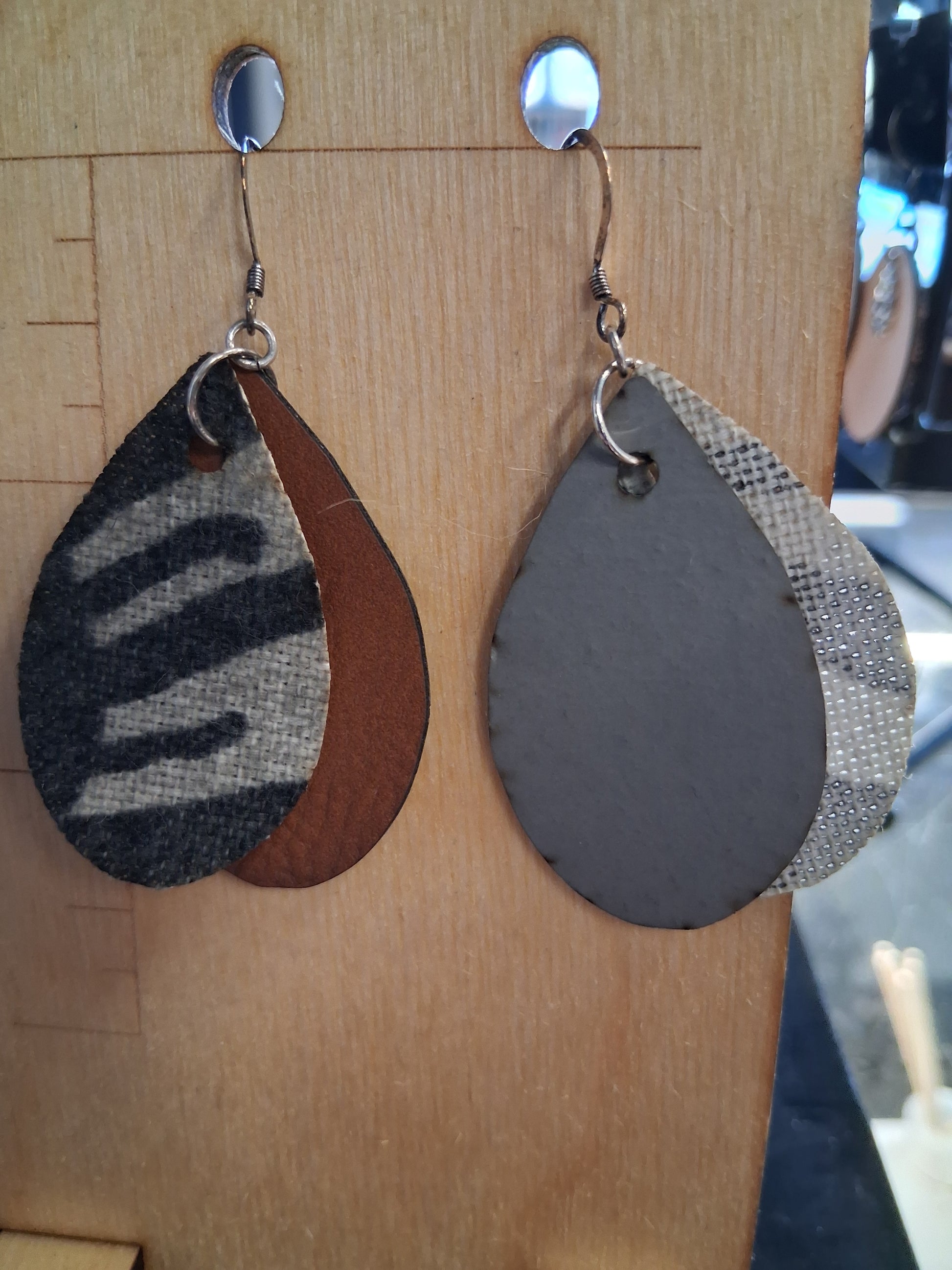 Pair of earrings with fabric in front of a pleather back on a wooden surface with a ruler for scale.